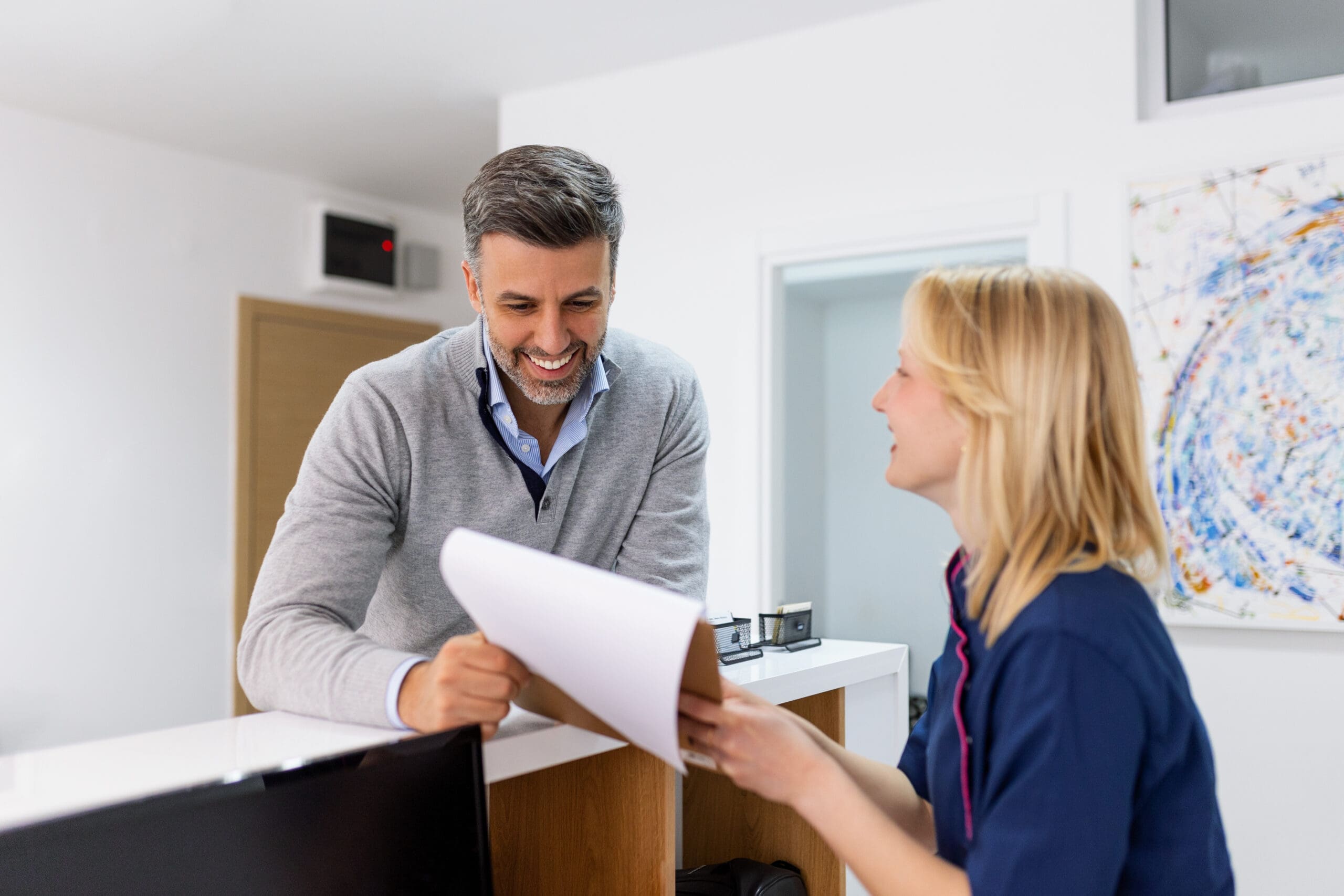 Man making an appointment with medical staffs at reception desk in hospital. Medical staff and nurse - receptionist talking to patient in front of the reception counter in hospital. Cleaner holding a plunger in front of toilet.